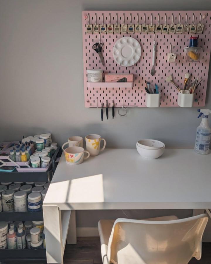 soft pink Ikea Skadis craft room ideas pegboard from @pots_by_potts_ with organized craft tools and white desk underneath sunlight shining in
