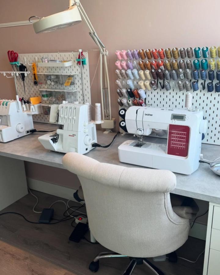 White pegboard with rainbow thread spools and sewing machines in a craft room from @madebyhole. Organized ikea skadis craft room ideas with color-coded thread storage.