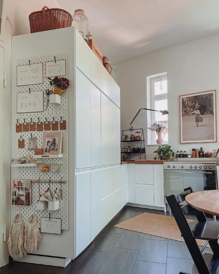 White Skadis pegboard with natural wood accents on kitchen cabinet by @uls_andthekids for ikea skadis craft room ideas, holding clips and hooks neatly organized