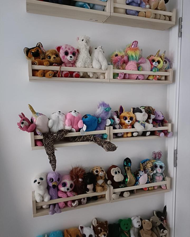 Light natural wood floating spice racks displaying colorful plush toys by Steph Reed in a tidy wall-mounted arrangement for creative small space storage
