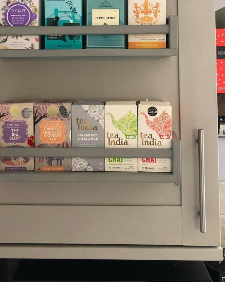 Gray wooden Ikea rack with slim horizontal rails holding colorful tea boxes from @maoko_angu. Neat and practical kitchen storage solution.