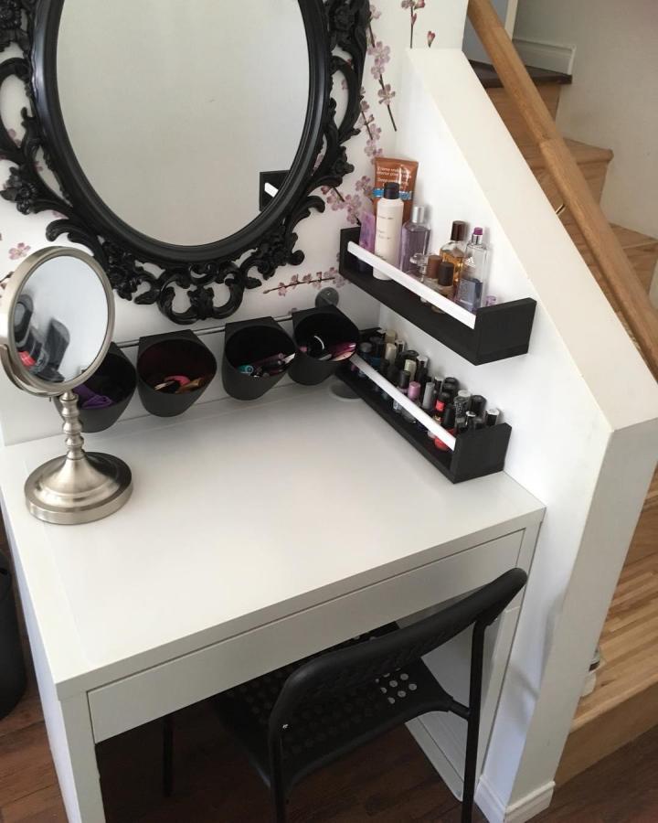 Black wall-mounted organizer with bottles and nail polish on white desk corner by @glitterandchocolate. Small space, neat styling, modern look.
