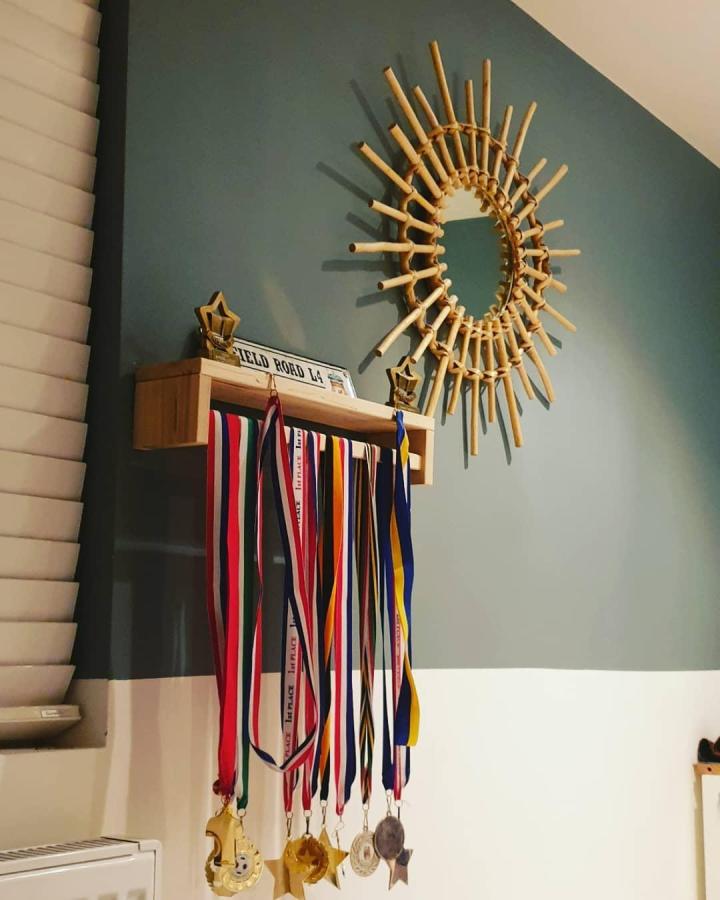 Light wood wall-mounted rack with hanging ribbons and medals by @the_pink_dore. Creative repurposing of kitchen storage for trophies.