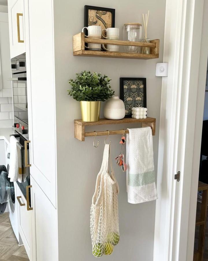 Light wood Ikea spice rack hack with gold hooks mounted on a pale wall showing hanging towels and bags by @newbuildhomediary.