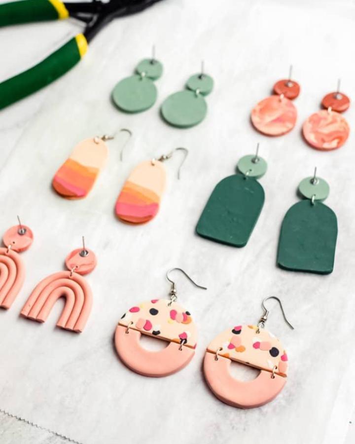 Muted green and pastel pink polymer clay earrings in geometric and speckled designs on white background by sarah maker. Playful handmade jewelry pieces.