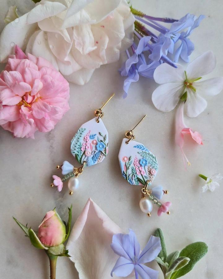 White polymer clay earrings with pastel floral patterns and dangling beads by @embellish.handmade. Elegant textured craft design.