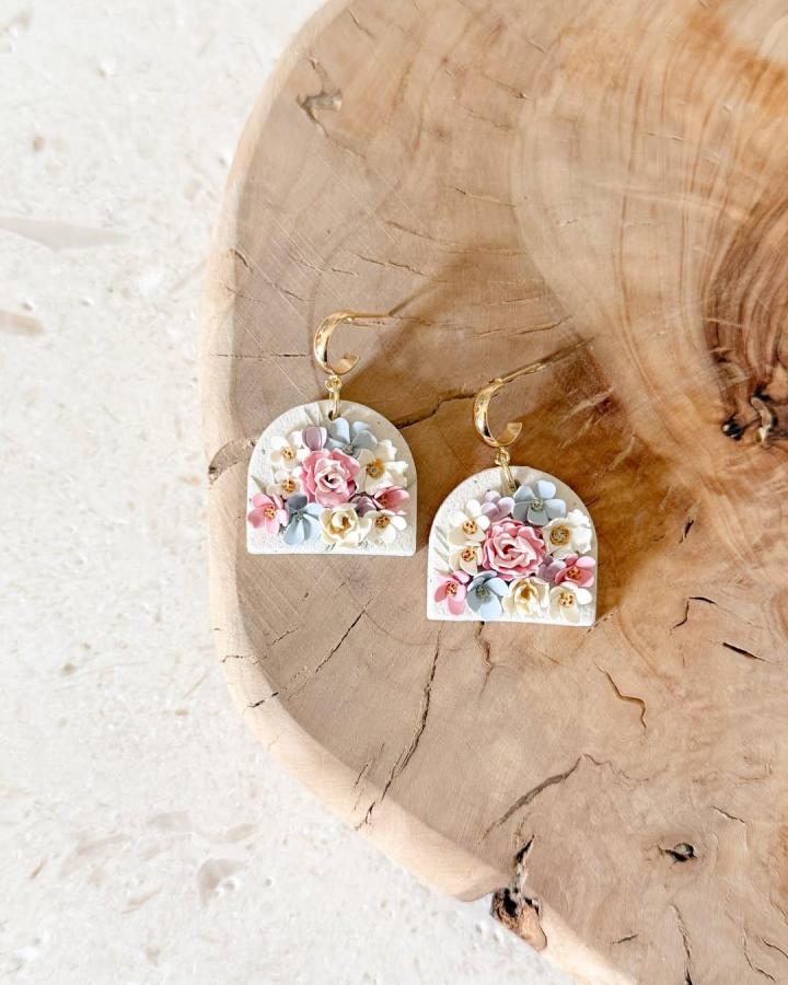 Delicate pastel floral polymer clay earrings with gold hoops on wooden surface by @desertclaydesigns. Soft colors and textured clay detail.