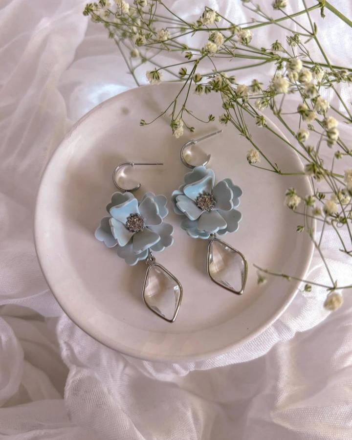 Soft blue floral clay earrings with silver hoops and clear crystal drops on white dish by @madremiadesigns. Elegant handmade accessory.