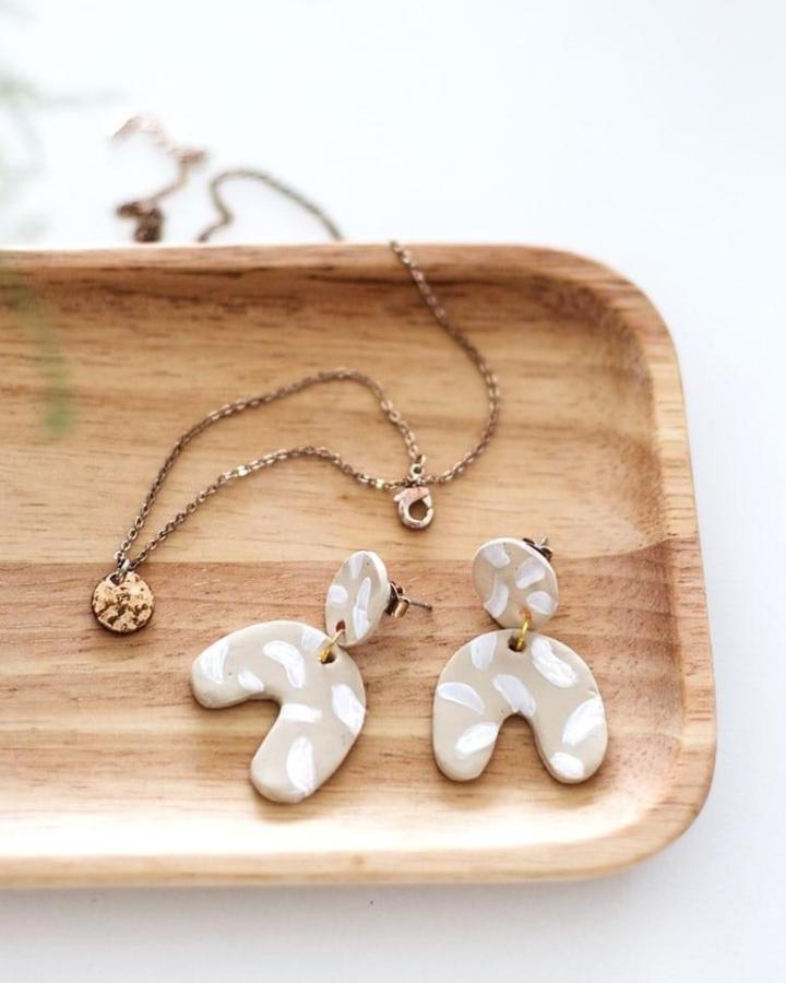 Beige polymer clay earrings with white brushstroke details on wooden tray from the lovely drawer showing playful abstract polymer clay earrings ideas.