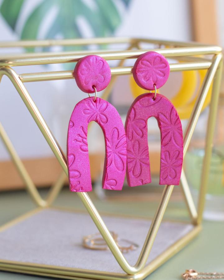 Bright fuchsia embossed floral polymer clay earrings hanging on a gold geometric stand showcasing polymer clay earrings ideas.