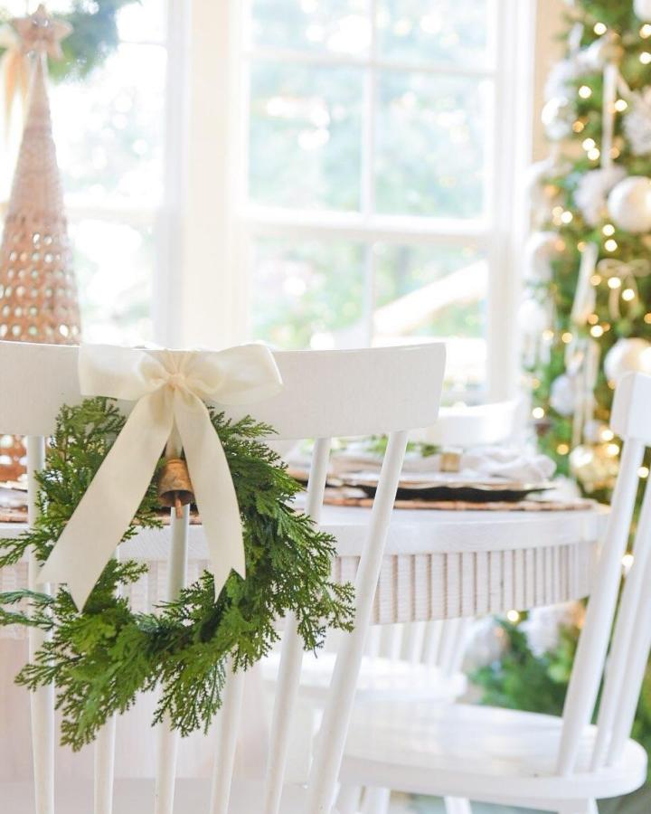 Soft ivory ribbon tied mini greenery wreath on white chair from @montgofarmhouse. Cozy festive chair decoration with natural textures and neutral colors.