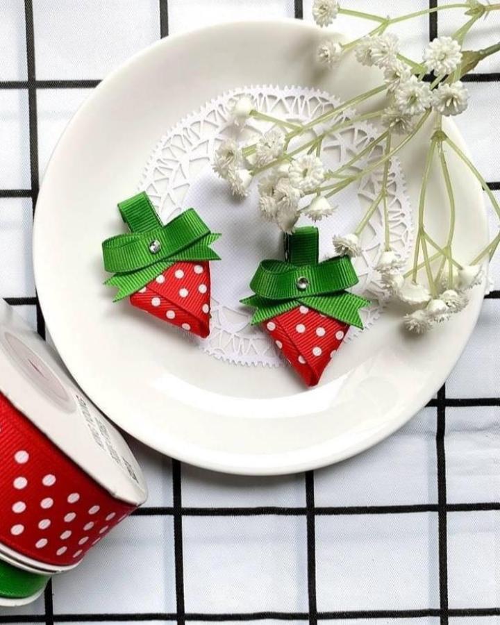 Red polka dot and green grosgrain ribbon strawberry-shaped hair clips with rhinestone details on white plate by @king_young_ribbon.