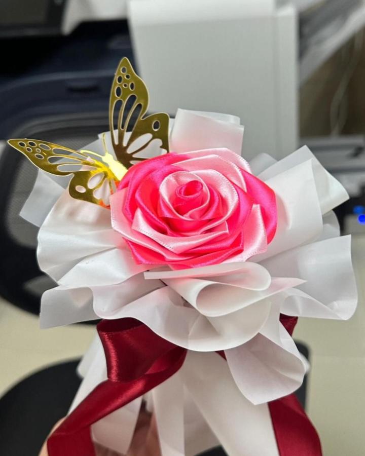Pink and white satin ribbon rose with red ribbon tails and a gold metal butterfly detail by @riyans.eternal.blooms, elegant handcrafted floral craft.