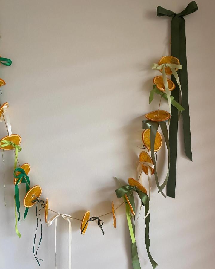 Dried orange slice garland with forest green, cream, and lime ribbons from @jklittleprojects hanging on wall for craft decor.