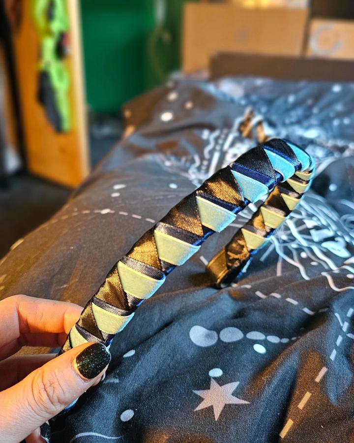 Black and blue woven satin ribbon headband held by hand on dark patterned fabric by @blue3clipse showing detailed handcrafted accessory.