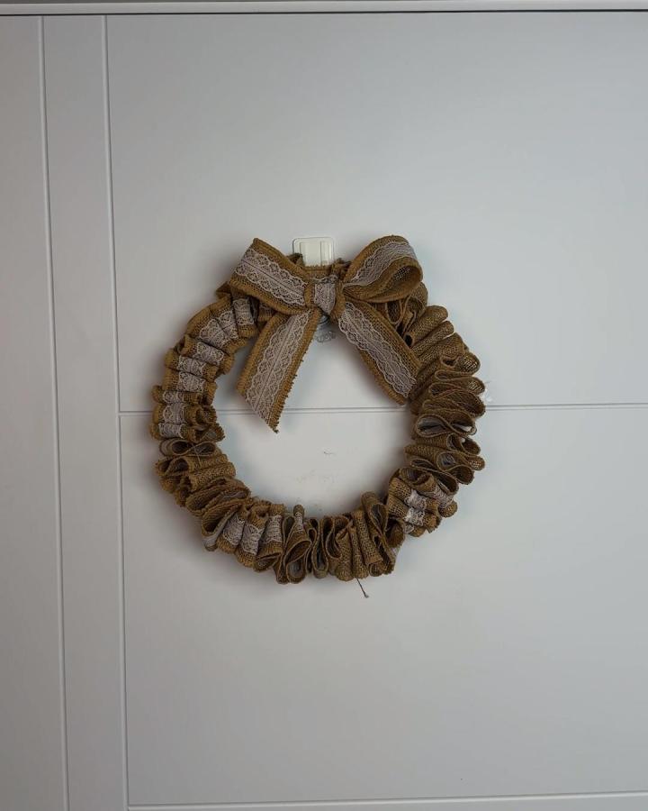 Rustic burlap and white lace ribbon wreath hanging on white wall from @beamishcreator showcasing handmade home decor craft idea.