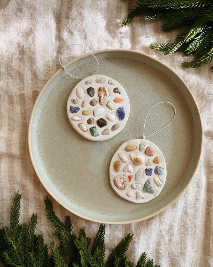 White clay discs with natural seashell and stone mosaic decorations on a ceramic plate from almost makes perfect. Coastal-inspired handcrafted ornaments with soft natural tones and textures.
