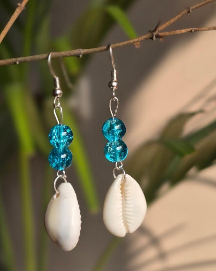 White cowrie shell earrings with bright turquoise blue beads hanging on silver hooks from @shellkrafts. Simple coastal jewelry with vibrant color contrast.