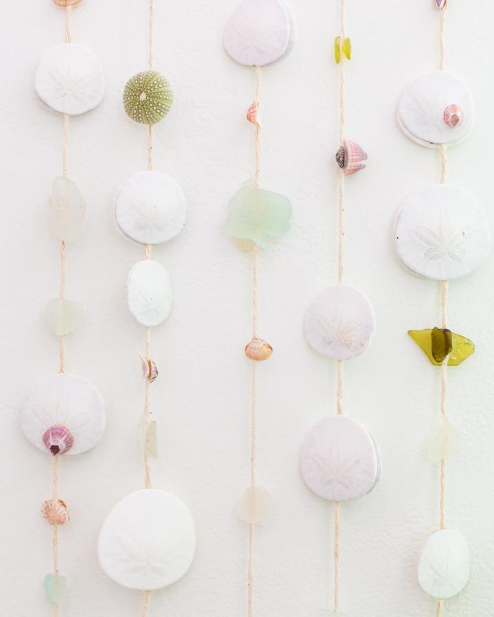 White sand dollars and sea glass hanging decor with tiny shells on twine. Coastal-inspired adult craft idea from lovely indeed. Soft, natural elements for wall art.