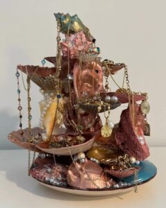 Pink and gold seashell jewelry holder adorned with chains and pearls by @sage.chabinsky.art. Artistic and elegant display piece.