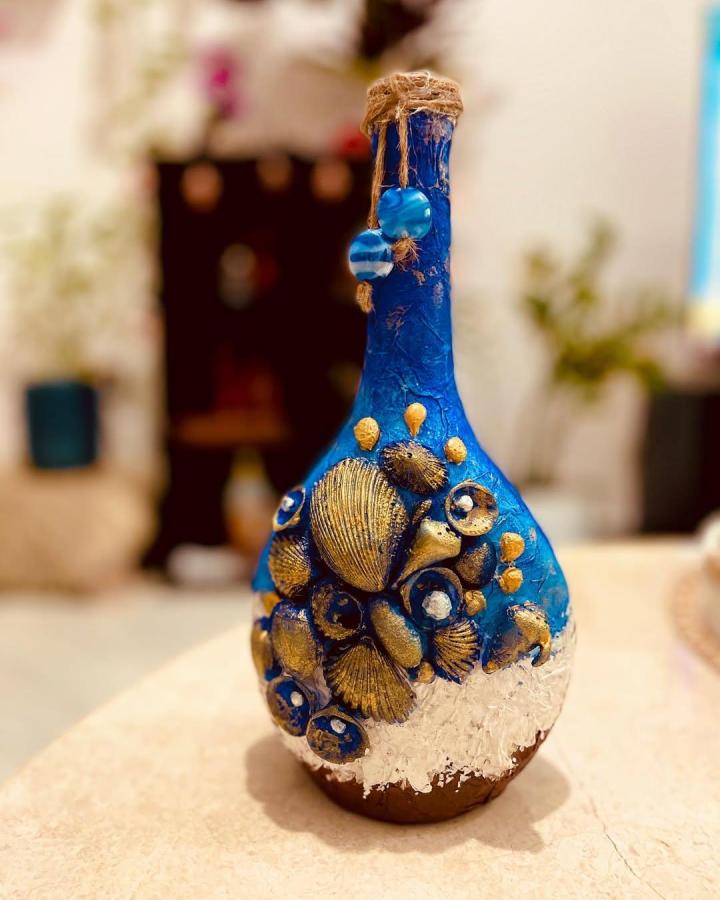 Bright blue decorative bottle with golden seashell embellishments and white textured base by @vismayavishnuprasad. Coastal craft with rustic glass bead accents.