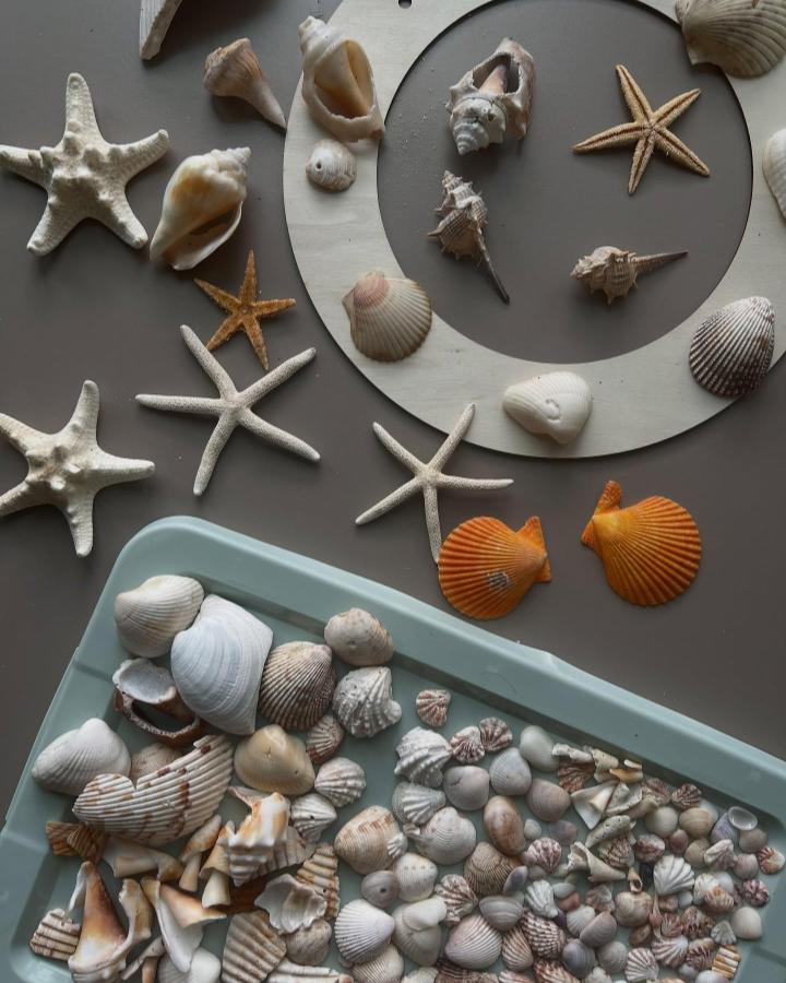 Light and muted natural shells arranged on a wooden ring base with starfish and scallops by @katerina.greshnova. Coastal-inspired home decor idea.