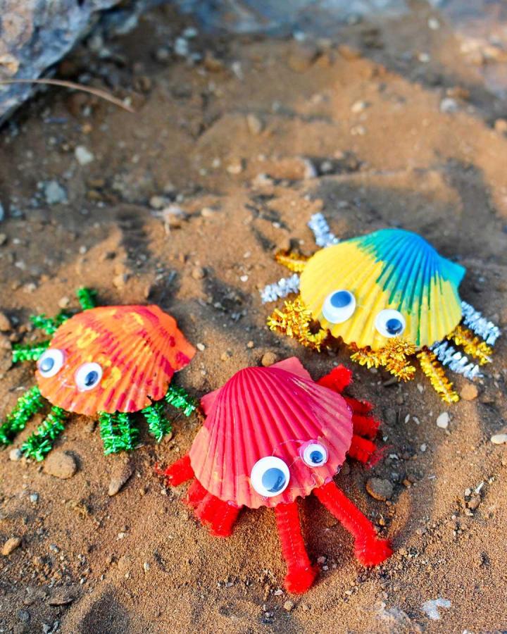 Brightly painted seashell crabs with colorful pipe cleaner legs and googly eyes on sandy surface craft idea from welcome to nanas playful coastal decor