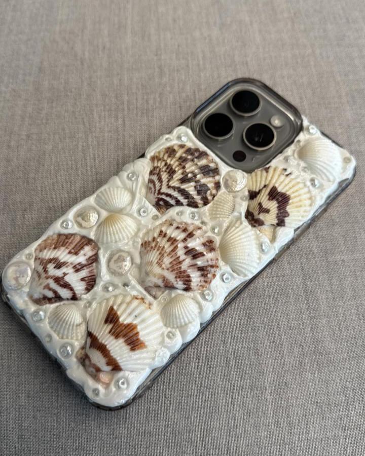 Seashell decorated phone case with natural brown and cream shells and pearl accents by @morgssgallery showcasing seashell crafts for adults.