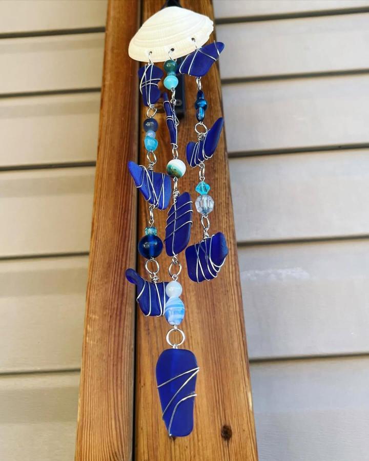Blue sea glass and bead wind chime with silver wire wrapping on natural shell top by @sandandsecreations, handmade coastal decor for outdoor spaces
