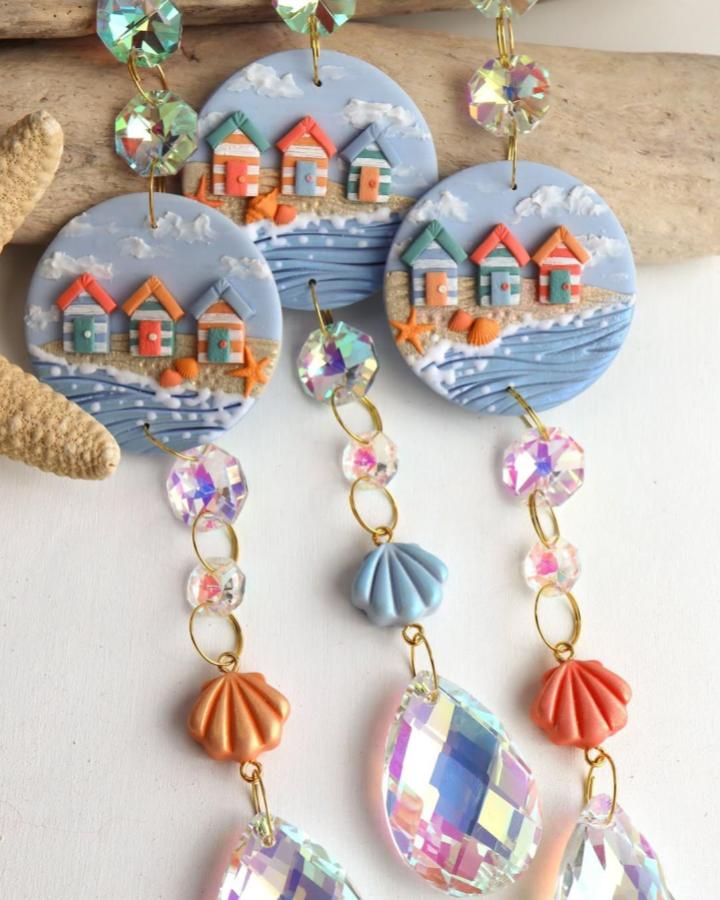 Blue and orange beach hut clay charms with iridescent beads and seashell motifs from @studiozero39. Summer-inspired craft accessory with coastal details.
