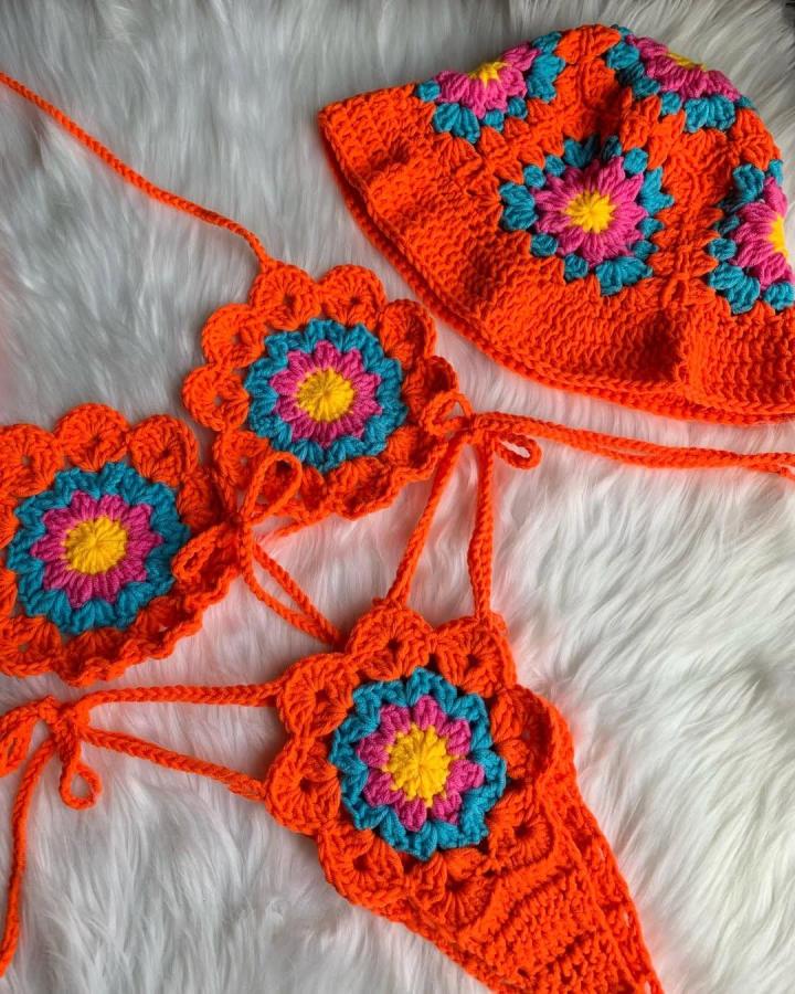 Bright orange crochet bikini and bucket hat with floral motifs on white furry surface by @wildxdandi. Handmade wearable art inspired by summer beachwear.