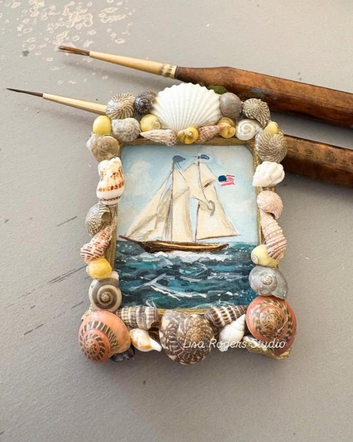 Seashell decorated frame with a painted sailboat and ocean waves, summer coastal crafting idea by @lisarogersstudio.