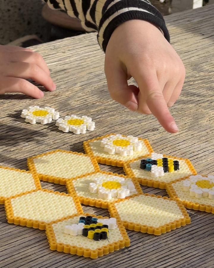Yellow and white Hama bead hexagonal coasters with bee and daisy designs on rustic wooden table summer activity.