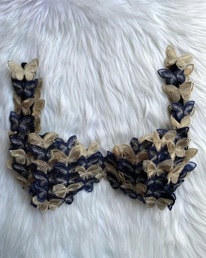 Butterfly embroidered lace bra on white fur background from @wildxdandi. Detailed summer wearable craft with navy and cream tones.