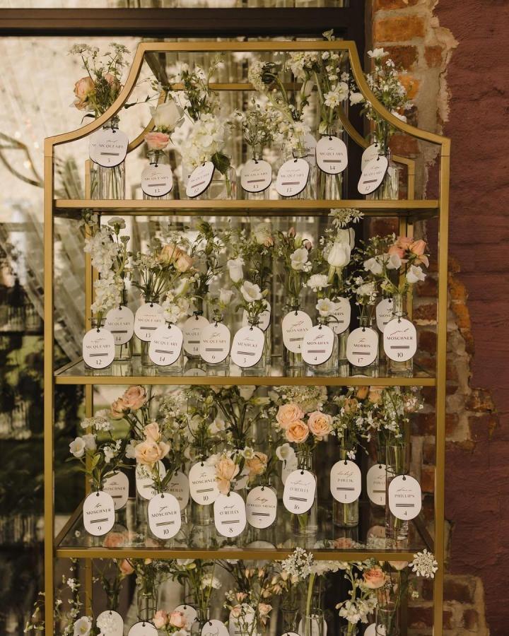 Soft peach and white floral bud vases with custom name tags on a gold shelf wedding favor ideas from @queencity.blooms. Elegant and personalized keepsakes for guests.