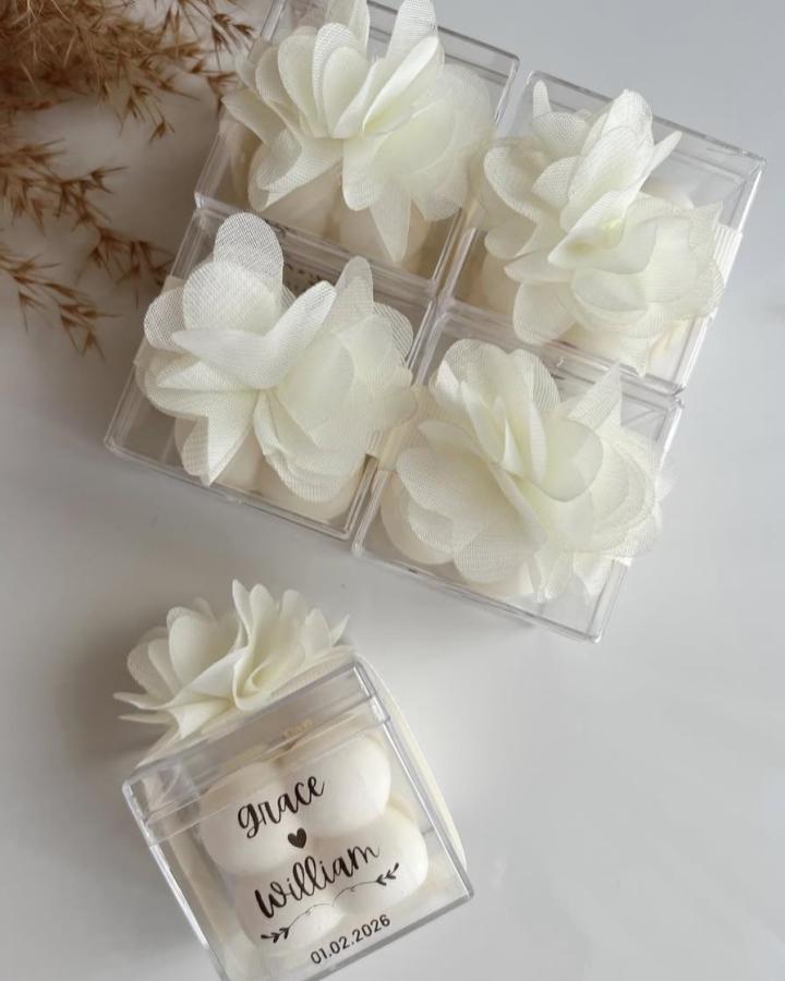 Clear personalized favor boxes with white fabric flowers and hand-poured bubble candles from @lalibu.atelier wedding favor ideas delicate and elegant design