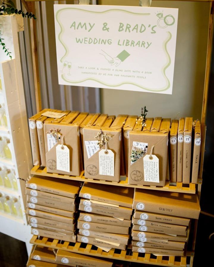 Brown paper wrapped books with tags and dried flowers from @amyslockdownlibrary wedding favor ideas display on wooden shelves.