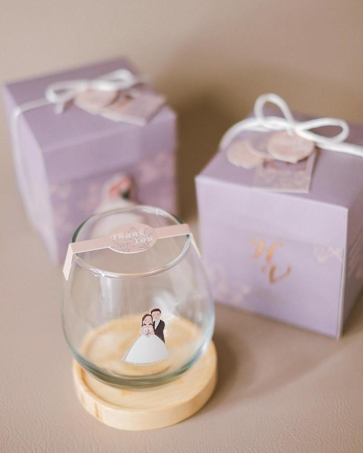 Lilac glass globe with wooden base and bride groom illustration from @celestia.gift wedding favor ideas. Elegant pastel gift box with ribbon and floral tag.