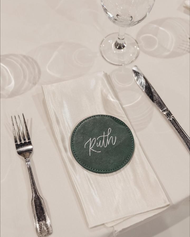 Green leather coaster with white script on folded napkin at place setting wedding favor ideas from @letter_zen. Elegant and practical gift choice.