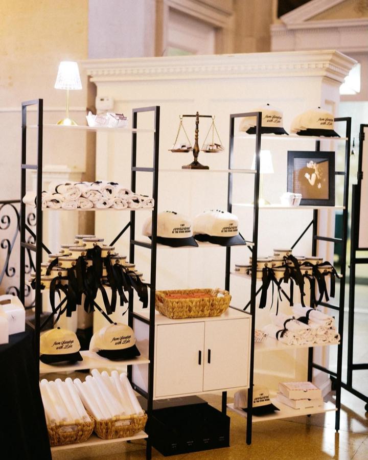 Neutral black and white pop up shop style shelving with wedding favor ideas from @themaineventbykelly featuring hats, towels, and small boxes.