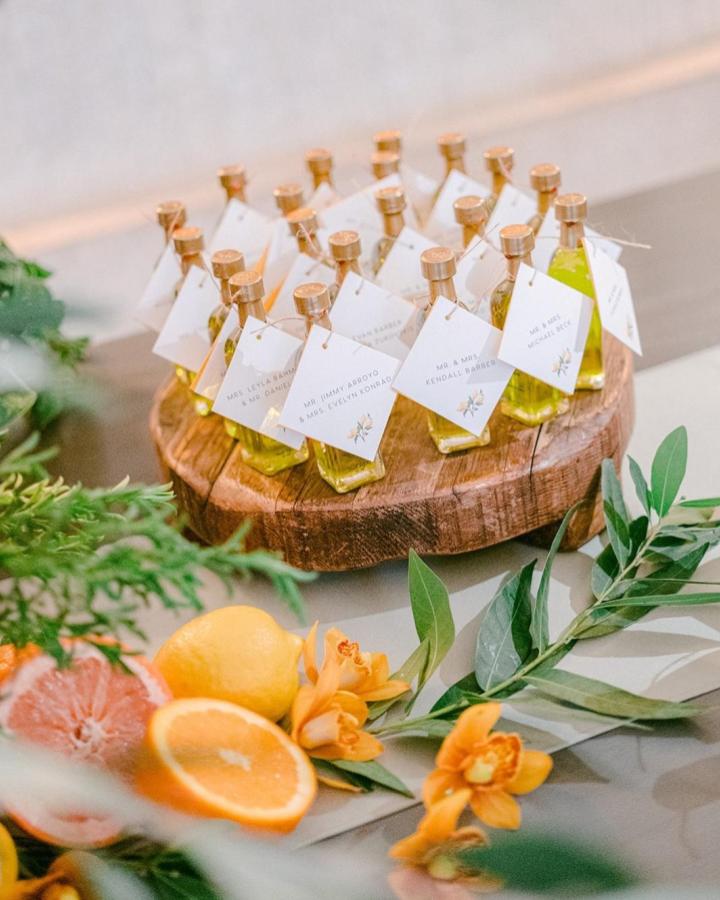 Mini olive oil bottles with personalized tags on wood slab from @infiniteevents_ wedding favor ideas with citrus and floral accents.