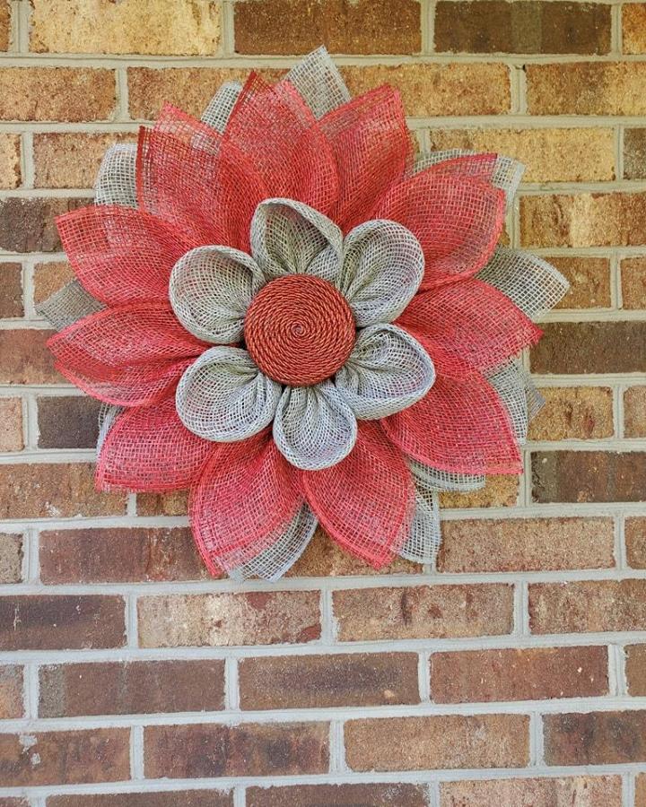Dusty red and gray burlap flower wall hanging with twisted rope center from @southernbcrafts_. Rustic layered floral décor on brick wall.