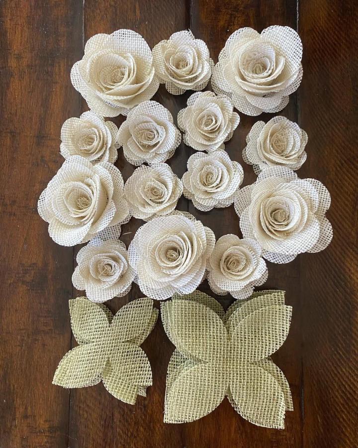 White burlap roses with green burlap leaves handcrafted by @jerseysilkiesdnalab on wooden surface showing rustic floral craft.