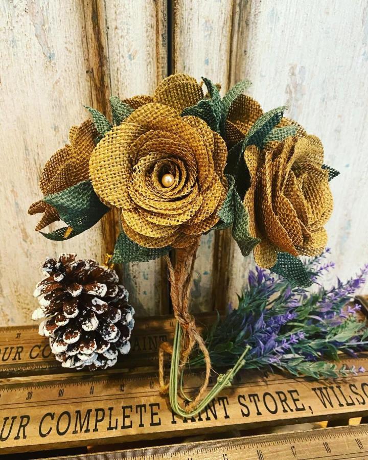 Golden mustard burlap flower bouquet with green leaves and twine handle from @jerseysilkiesdnalab. Rustic, textured handmade floral arrangement.