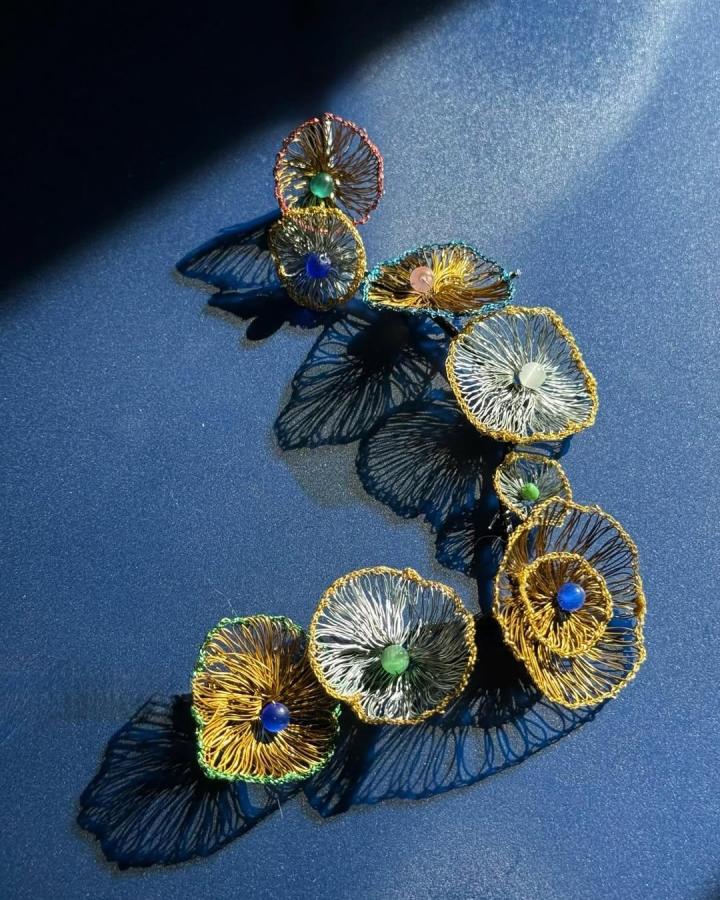 Copper and gold wire crochet flowers with colorful bead centers from @lixu829 casting intricate shadows on a blue surface.
