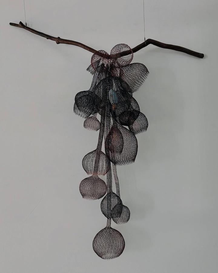 Hand knitted copper wire sculpture hanging from natural branch by @nettiesumner featuring airy mesh bubbles in dark metallic tones.