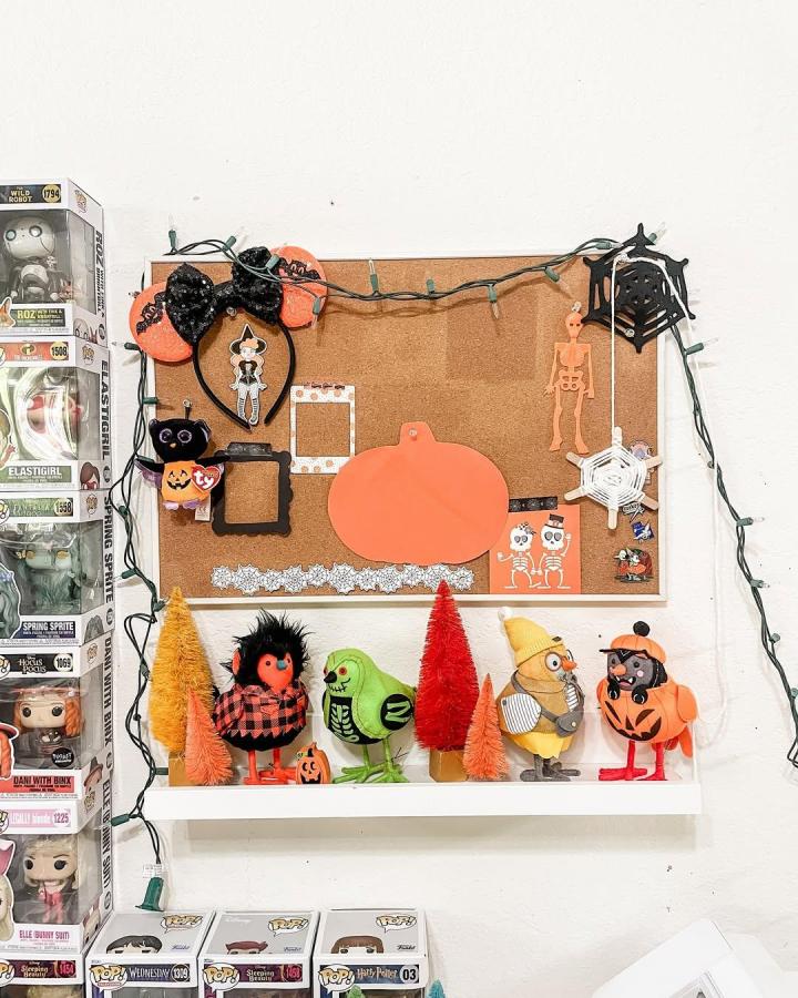 Orange and black festive cork board craft by @mrsscrapandplan with Halloween decorations and string lights on a white wall.