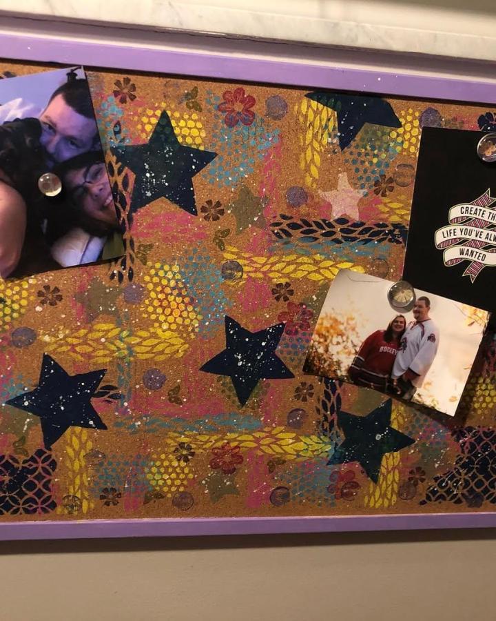 Colorful mixed media cork board with painted star stencils and purple frame by @i.am.enough_christina holding pictures and notes.
