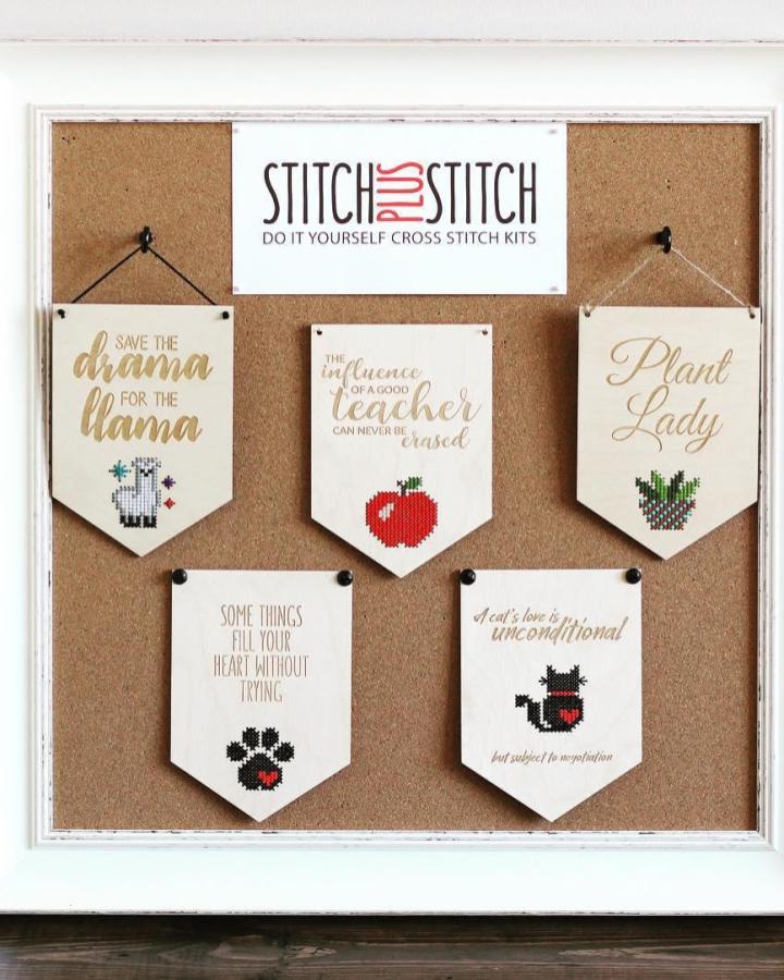 White framed cork board craft display organizer from @stitch_plus_stitch with charming cross stitch banners and witty quotes pinned.