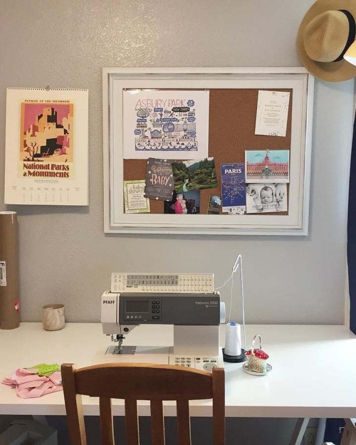 White framed cork board over sewing desk with travel postcards and baby photos from @emmas_crafternoons. Cozy craft wall organization.